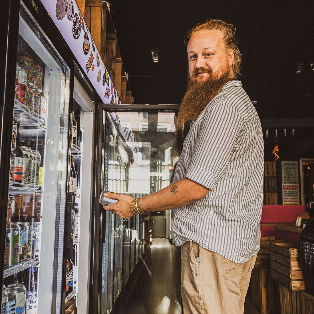 Ewoud Ruesink met een blik bier in de hand bij de koelkasten van zijn bierwinkel