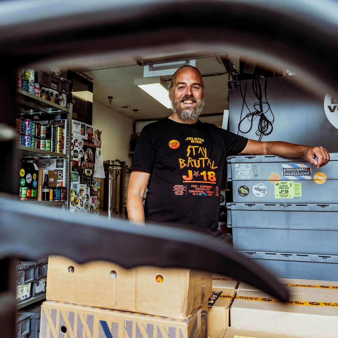Jelle Peddemors lachend in zijn garagebrouwerij tussen kratten en bierblikken
